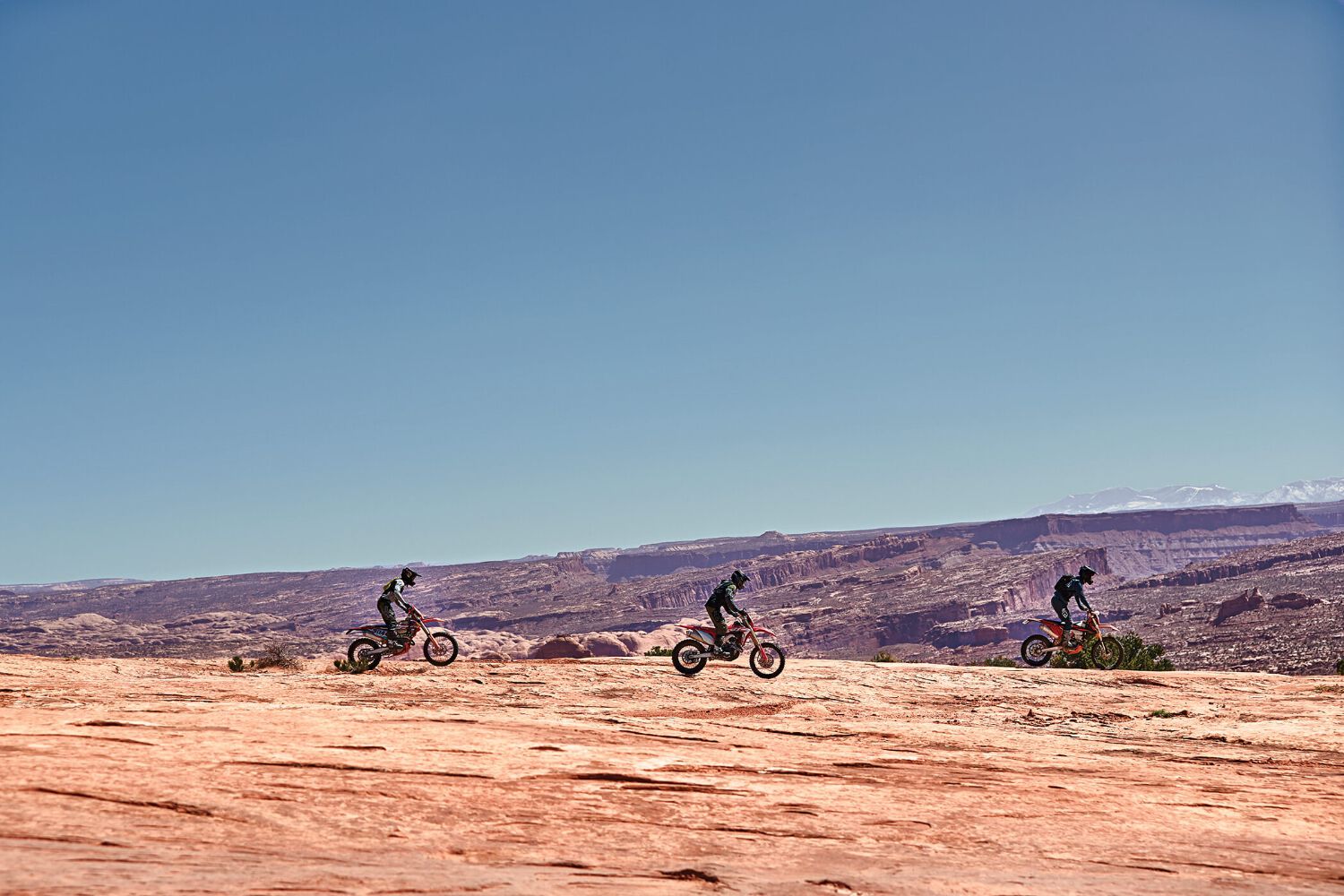 Three dirt biking riding in a line, following one by one.